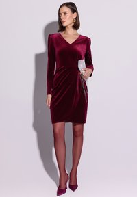 Burgundowa aksamitna sukienka z dekoltem w serek, długimi rękawami i marszczeniem po boku. Do tego srebrna kopertówka i pasujące wysokie obcasy.