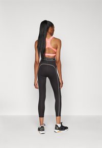 Leggings neri con piping bianco ai lati, abbinati a un reggiseno sportivo rosa con un design a cut-out sulla schiena. Scarpe da ginnastica completano l'outfit.