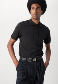 Svart polo skjorte med klassisk krage, korte ermer og en treknapps placket, kombinert med stripete bukser og et teksturert svart belte.