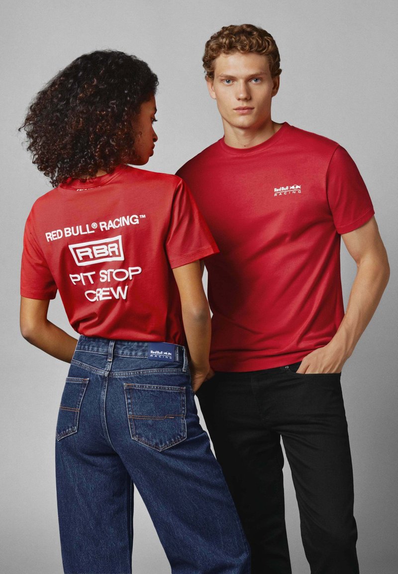 Røde t-shirts med korte ærmer med teksten "RED BULL RACING" og "PIT STOP CREW". Blå denim jeans med baglommer. Glatte teksturer; enkelt design.