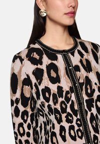 Beige, schwarze und braune Strickjacke im Leopardenmuster mit rundem Ausschnitt und schwarzen Knopfakzenten, die kontrastierende Stickdetails aufweist.