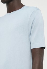 Ανοιχτό μπλε πλεκτό κοντομάνικο μπλουζάκι με στρογγυλή λαιμόκοψη, λεία υφή και διπλωμένα τελειώματα στα μανίκια. Κατασκευασμένο από απαλό, ελαστικό υλικό.