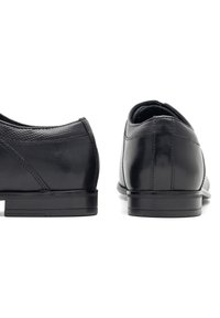 Czarne skórzane buty o gładkim i teksturowanym wykończeniu, z niskim obcasem i elegancką sylwetką. Minimalistyczny design z delikatnymi detalami szycia.