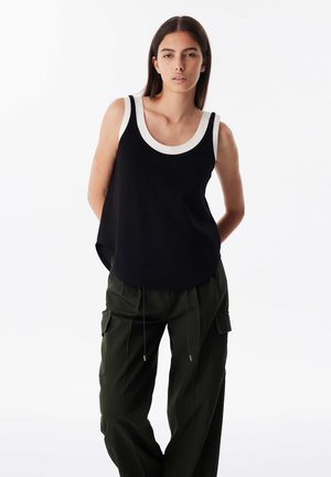 Schwarzes ärmelloses Oberteil mit einem kontrastierenden weißen Halsausschnitt, locker geschnitten und mit einem abgerundeten Saum, kombiniert mit grünen Cargo-Hosen.