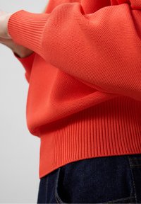 Heldere oranje gebreide trui met ribboorden en zoom, textuurstof en een relaxed fit, gecombineerd met donkere blauwe denim jeans.