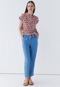 Blommig kortärmad blus med röda, blå och vita mönster. Ljust blå tajta byxor med elastisk midja. Beigefärgade vävda sandaler.