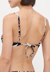 Črn cvetlični bikini vrh z nastavljivimi naramnicami. Ima zavezovanje na hrbtu in barvite tropske vzorce na gladki tkanini.