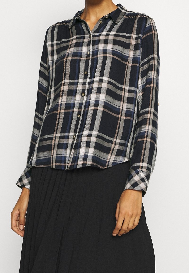Chemise à carreaux navy à manches longues avec un col, coupe décontractée, et boutons dorés. Tissu doux avec un motif à carreaux.