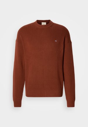 Ruskeanvärinen ribattupusero pyöreällä kaula-aukolla, jossa on pieni logo rinnassa ja rento malli. Valmistettu teksturoidusta neuloksesta.