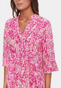 Rosa mönstrad klänning med V-ringning, trekvartsärmar och volangmanschetter. Har abstrakta vita och mörkare rosa former genom hela plagget.