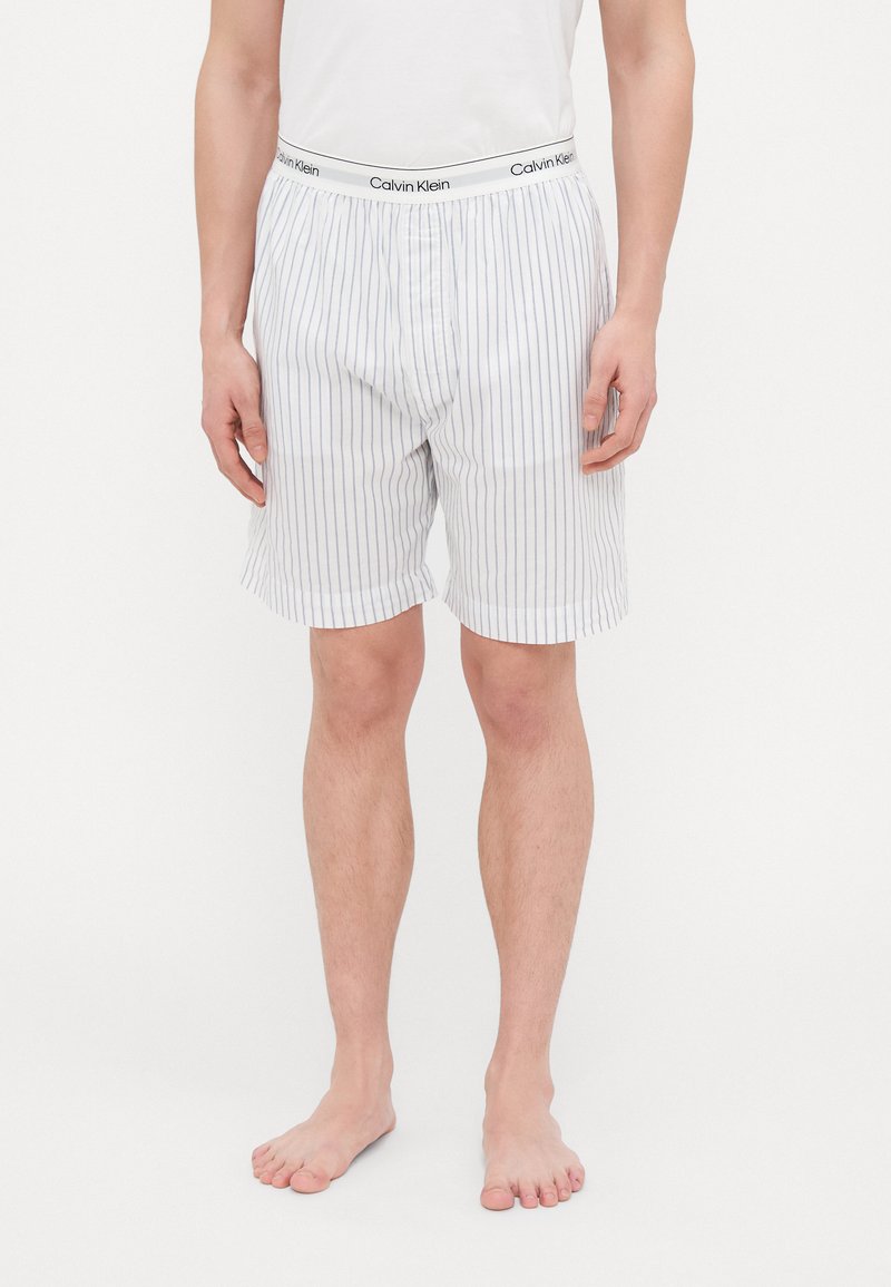 Hvite bomullsbokser med blå vertikale striper. Har en svart Calvin Klein-logo på midjebåndet. Avslappet passform, pustende stoff.
