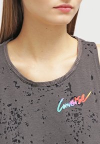 Camiseta sin mangas gris con patrón salpicado, escote redondeado y ribetes acanalados. Presenta un colorido logo de "Converse" en colores degradados en el pecho.