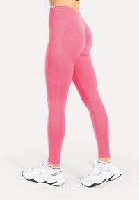 Różowe legginsy wykonane z elastycznego materiału, z wysokim pasem i dopasowanym krojem. Połączone z białymi trampkami i czarnymi akcentami.