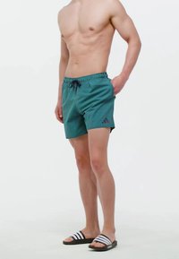 Bañador turquesa con rayas verticales, cinturilla elástica y cordón. Presenta un logo de adidas en negro en la pierna izquierda.