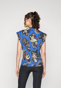 Haut sans manches bleu avec un motif de papillon ; présente des couleurs vives, un col rond et une coupe décontractée. Le matériau semble lisse et léger.