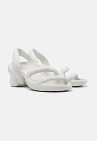 White sandals with a flexible, sculptural design. Features curved straps and a thick, rounded sole. Made of a smooth, rubber-like material.