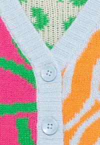 Cardigan lavorato a maglia colorato con motivi rosa e verde, accenti arancioni e bordo a coste blu chiaro con bottoni sulla chiusura a V.