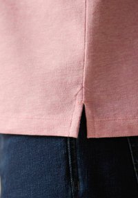 Camiseta de algodón rosa con un acabado texturizado, que presenta una abertura lateral en el dobladillo y se combina con jeans de mezclilla oscura.