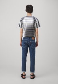 Camiseta de algodón a rayas en azul marino y blanco, combinada con pantalones de mezclilla de corte recto, con bolsillos laterales y puños enrollados.