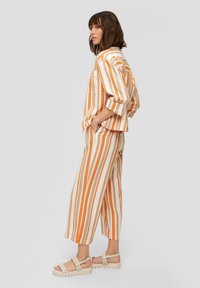 Gestreepte katoen blouse in oranje en crèmewit, gecombineerd met bijpassende wijde broek. Met opgerolde mouwen en gevlochten sandalen met een sluiting.