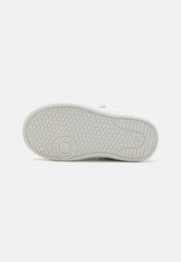 Semelle de sneaker blanche avec un motif de grip texturé, présentant un logo circulaire et des bords légèrement arrondis pour le confort et la traction.