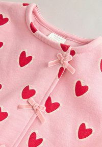 Rosa kofta med röda hjärtmönster, rund halsringning och små sammetsrosetter som knäppning längs framöppningen. Mjuk textur.