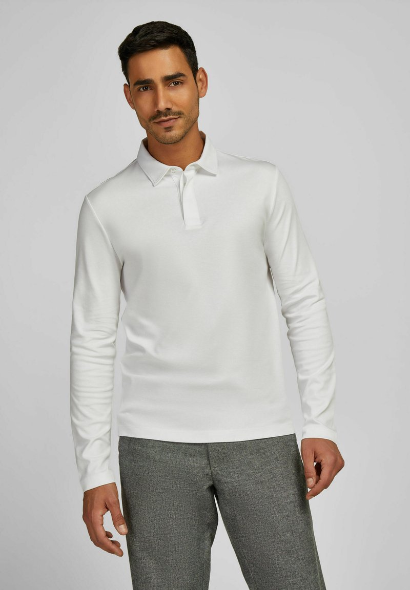 Langärmliges weißes Poloshirt mit spitzem Kragen und Knopfleiste, kombiniert mit strukturierten grauen Hosen, die einen maßgeschneiderten Look präsentieren.