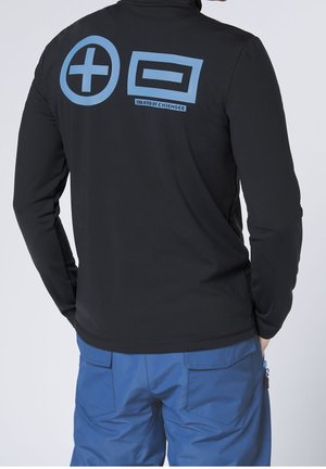 Osoba nosząca czarną bluzkę z długim rękawem z niebieskimi okrągłymi znakami plus i prostokątnymi znakami równości oraz niebieskie spodnie z tylnymi kieszeniami.