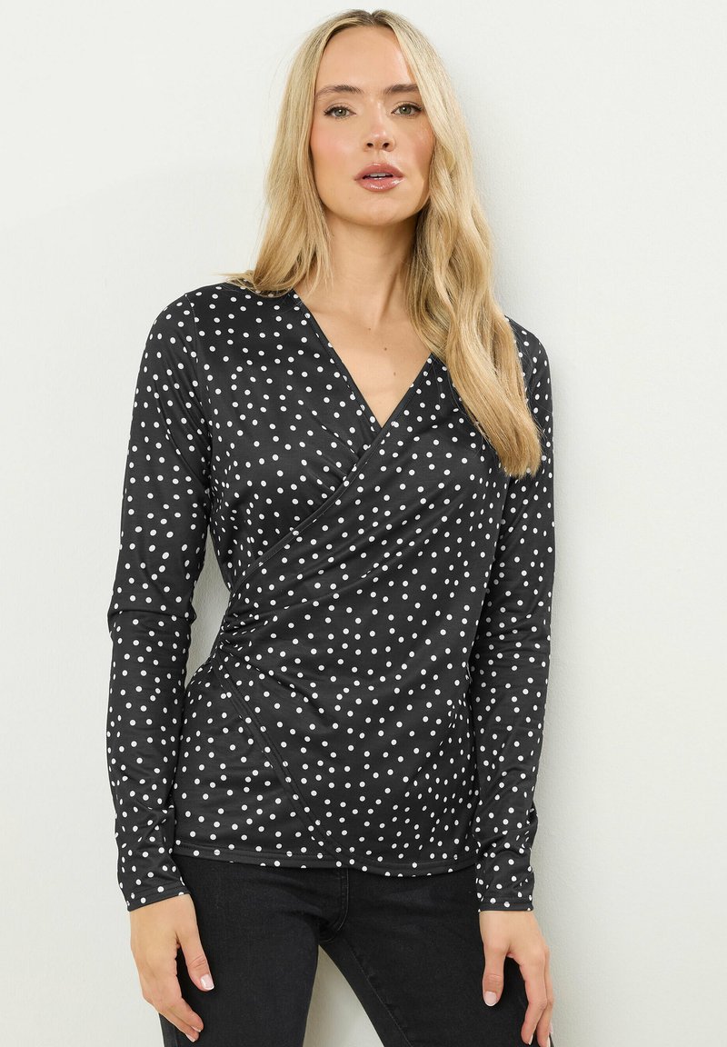 Zwarte lange mouwen wikkelblouse met witte stippen, voorzien van een V-halslijn en een aansluitende pasvorm. Soepele stof met een lichte rek.
