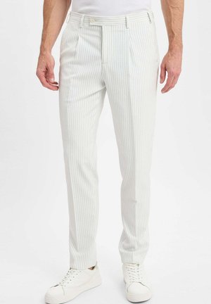 Witte broek met fijne krijtstrepen en een getailleerde pasvorm, met een platte voorkant en subtiele blauwe strepen. Gecombineerd met witte sneakers.