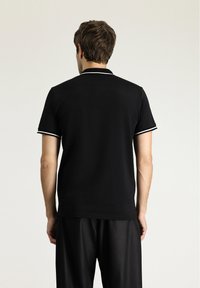 Polo nero con bordo bianco su colletto e maniche, maniche corte, realizzato in un tessuto liscio, design aderente e senza loghi visibili.