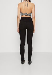 Jeans negros de cintura alta y un top halter cropped con un patrón de cuadros en blanco y negro, mostrando un diseño atado en la parte posterior.