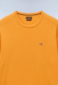 Maglione in lana merino di un brillante arancione. Presenta un colletto rotondo e un piccolo dettaglio ricamato della bandiera norvegese sul lato sinistro.