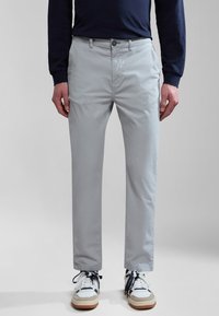 Pantalones de algodón gris claro con un corte ajustado, que cuentan con un cierre de botón y bolsillos laterales. Combinados con zapatillas blancas con acentos en azul marino.
