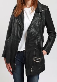 Černá kožená biker bunda s přiléhavým střihem, asymetrickým zipem, velkými kapsami a stříbrným páskem jako ozdobou. Hladká textura.