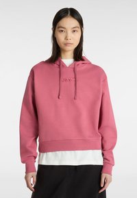 Rosa kortärmad huvtröja i mjukt tyg, med en känguruficka och snörning. Broderad logotyp på framsidan.