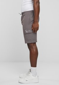Shorts cargo gris avec une taille élastique, des poches latérales et un patch logo. Associés à des baskets blanches et des chaussettes de longueur chevilles.