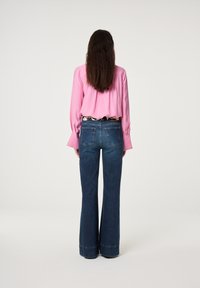 Roze blouse met lange mouwen, ingestopt in hoog-waisted blauwe flared jeans. Denim heeft een zachte textuur en subtiele vervaging. Aangepaste zwart-witte riem.