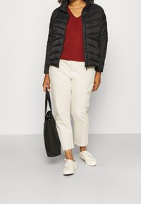 Schwarze Puffjacke, roter gestrickter V-Ausschnitt-Pullover, off-white cropped Pants, weiße Sneaker und eine schwarze Tote-Bag. Glatte und strukturierte Materialien.