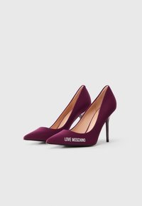 Vijolične visoke pete z ostrim prstom in elegantno silhueto, mehkih materialov ter logotipom "LOVE MOSCHINO" ob strani. Dizajn stiletto pete.
