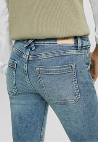 Ljusblå denimjeans har en åtsittande design med två bakfickor, förstärkta sömmar och en brun läderetikett märkt "ESPRIT."