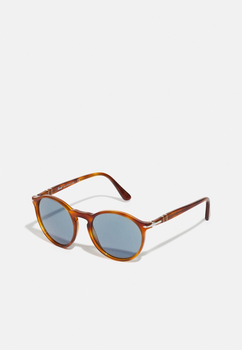Occhiali da sole rotondi con montatura in tartaruga, lenti blu e dettagli in metallo sulle astine. Finitura texturizzata, design leggero.