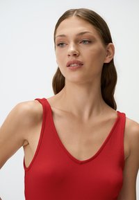 Top senza maniche a costine rosso con scollatura a V profonda e spalline larghe, caratterizzato da una texture liscia e un design aderente che si adatta al corpo.
