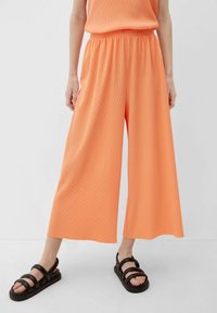Oranje, wijde broek van ribbelstof met een elastische tailleband. G gedragen met zwarte, strap sandaal op een neutrale achtergrond.