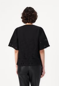 Black blouse with short puff sleeves, featuring floral embroidery and scalloped edges. Made from textured fabric with cut-out details.