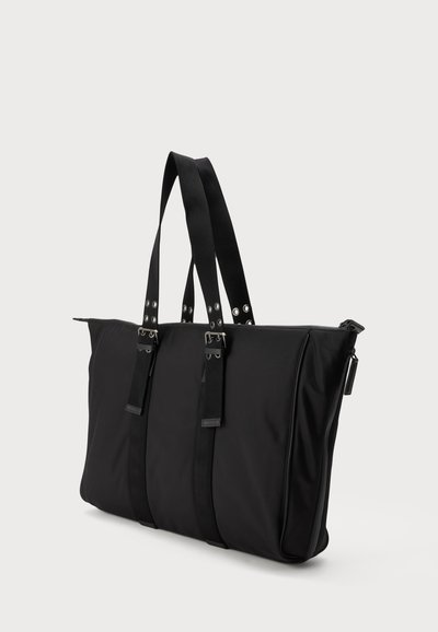 Sac cabas rectangulaire noir avec deux longues anses et des détails de boucles argentées, présenté sur un fond clair uni.
