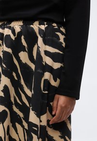 Close-up of person’s hand resting by side wearing black long sleeve top and beige skirt with bold black abstract print and elastic waistband.