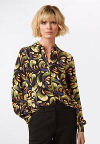 Blusa a maniche lunghe con colletto, caratterizzata da un motivo vorticoso multicolore in verde, arancione e viola su sfondo nero; chiusura con bottoni.