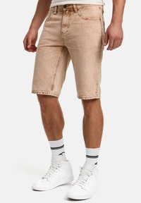 Shorts en jean beige avec légère décoloration, cinq poches et passants pour ceinture. Assortis à des baskets montantes blanches et des chaussettes rayées noires.