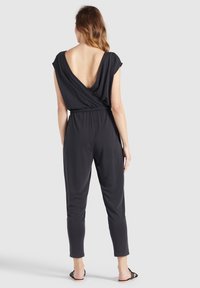 Zwarte losse jumpsuit met een diepe V-rug, korte mouwen, elastische taille en taps toelopende pijpen, gemaakt van glad, lichtgewicht materiaal.
